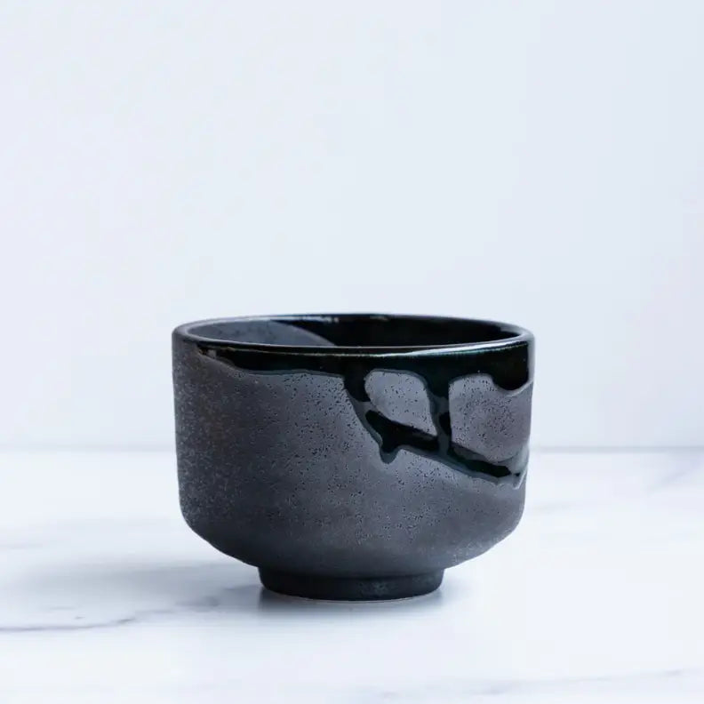 Tea-making set with a black box, matcha tea, mug, whisk, and chocolate on a white background