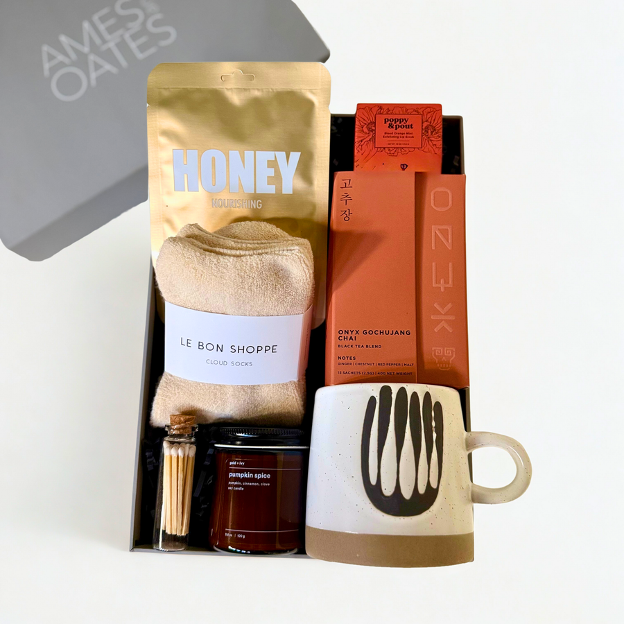Cozy gift box with le bon shoppe socks, candle, matches, chai tea, stoneware mug, Lapcos face mask, and poppy and pout lip scrub