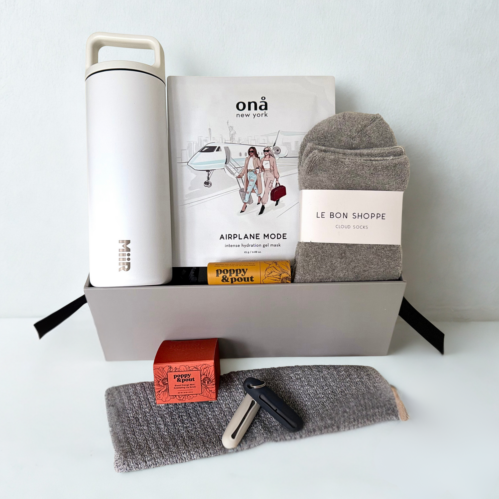 Collection of travel-themed products including a water bottle, socks, face mask,  lip balm/scrub, ear plugs