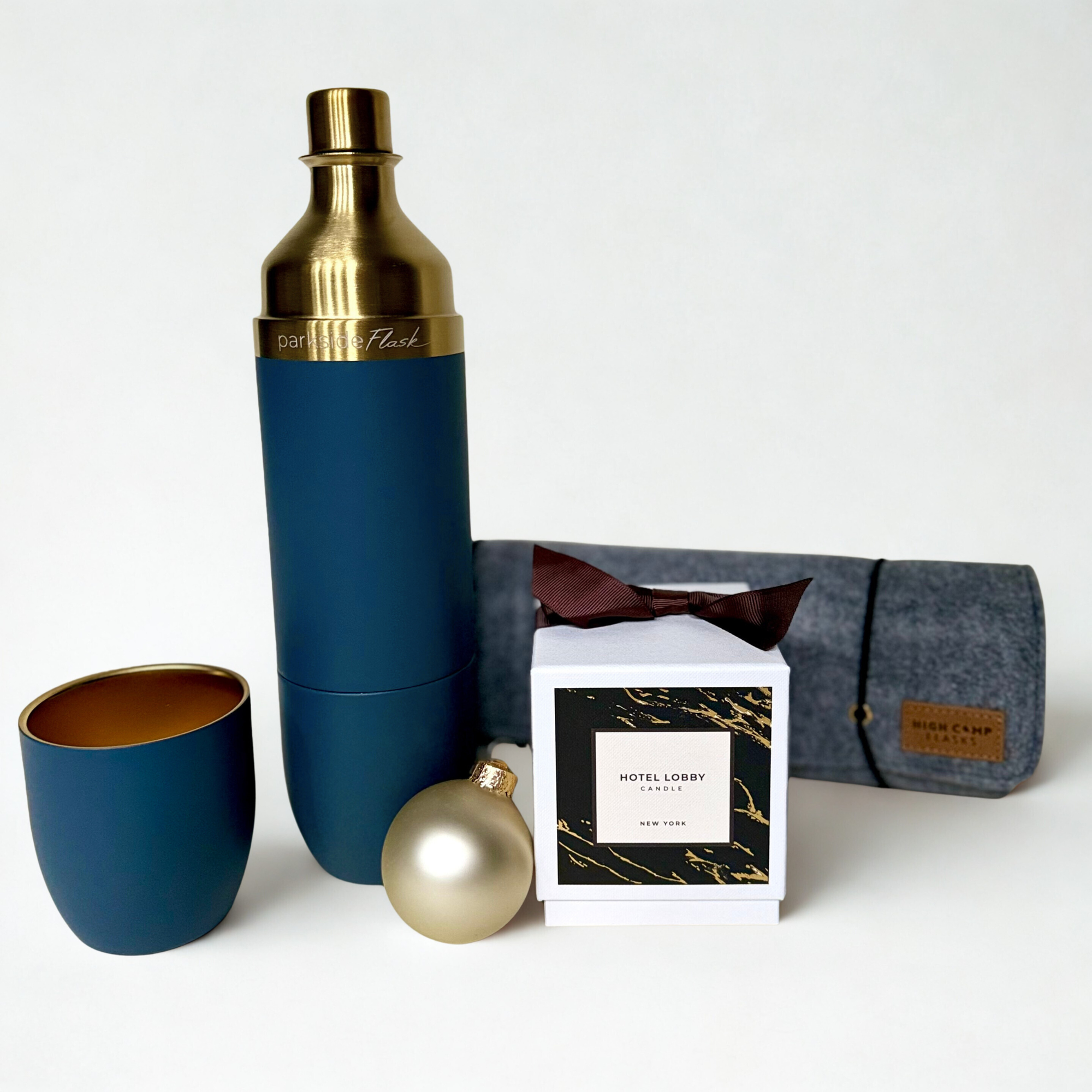 Blue and gold thermos with a cup, carry case, and candle, ornament, and gift box on a white background