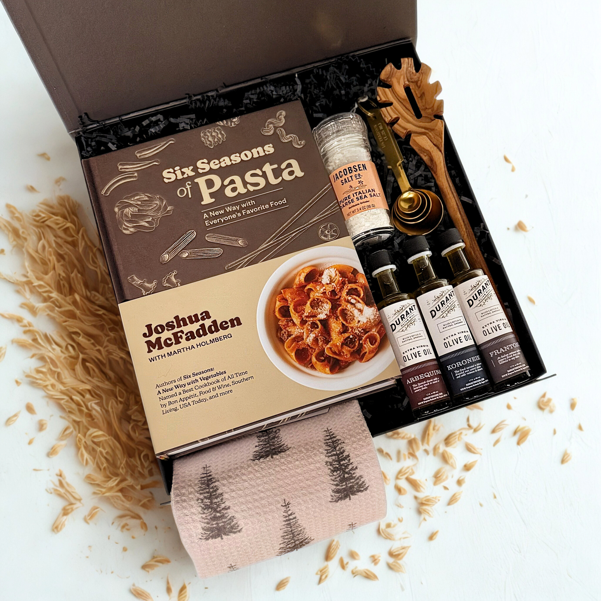 Gourmet gift set with pasta book, olive oil, italian salt, olive wood pasta spoon, tea towel, gold measuring spoons on a white background