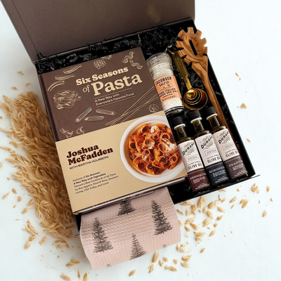 Gourmet gift set with pasta book, olive oil, italian salt, olive wood pasta spoon, tea towel, gold measuring spoons on a white background