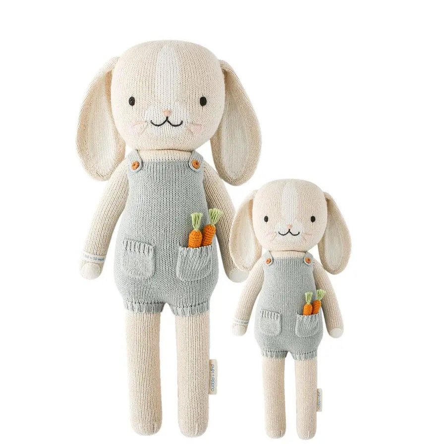 Hand made knitted toy rabbit in overalls with a blanket, silicone teething toy and sound machine on a white background